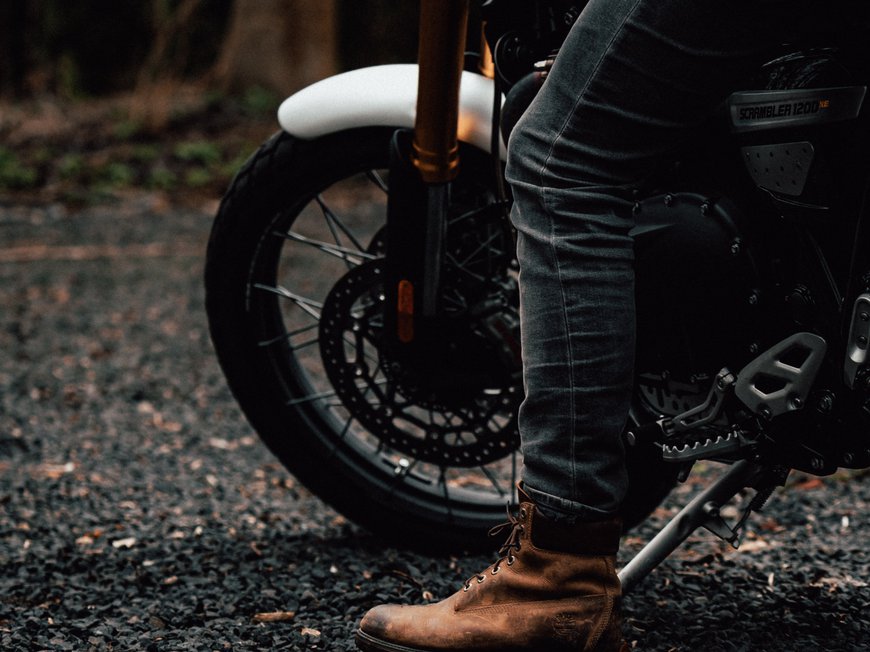 Hotel Böhlerstern: Motorradhotel in der Steiermark Bein mit braunem Stiefel neben schwarzem Motorrad auf Kiesboden