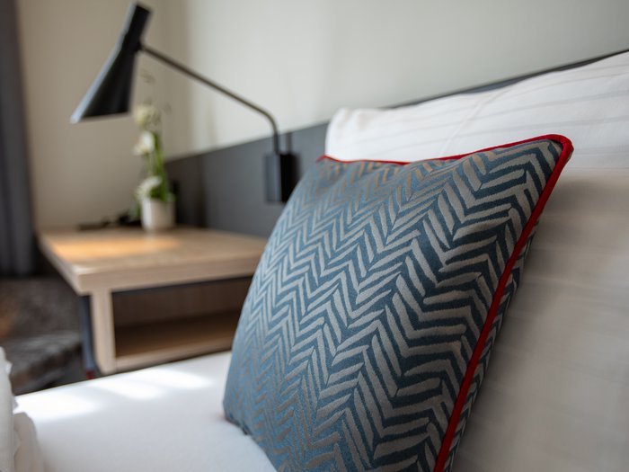 Hotel Böhlerstern in der Steiermark: unsere Zimmer Blau gemustertes Kissen mit rotem Rand auf einem weißen Bett im Hotelzimmer