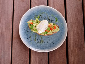 Restaurant Bachstelze in Kapfenberg Avocado-Toast mit gewürfelten Tomaten und pochiertem Ei auf blauem Teller
