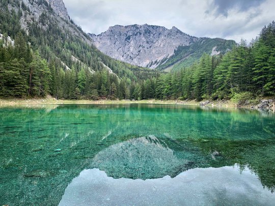 Our tips: the best trips in Styria Clear mountain lake reflecting fir trees and grey mountains under cloudy sky