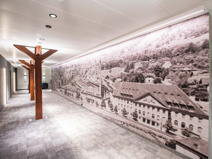 Hotel Böhlerstern in der Steiermark: unsere Zimmer Flur mit Wandbild einer alten Stadt und Holzbalken in modernem Gebäude