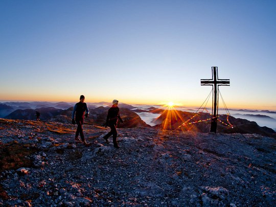 Our tips: the best trips in Styria Two hikers reach summit cross at sunrise in the mountains