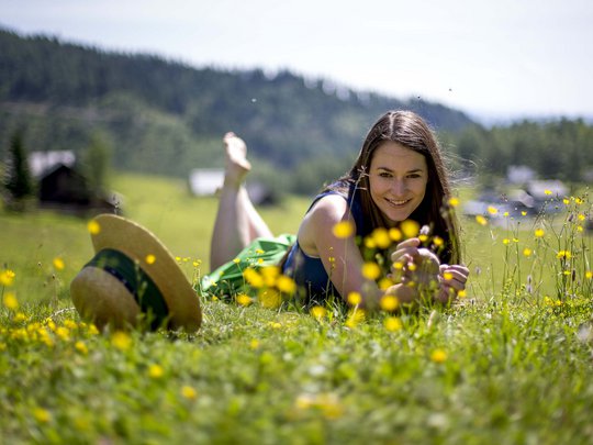 Our tips: the best trips in Styria Woman lying in a meadow with yellow flowers, mountains and houses in the background