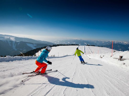 Our tips: the best trips in Styria Two skiers skiing down a snowy mountain slope on a sunny day