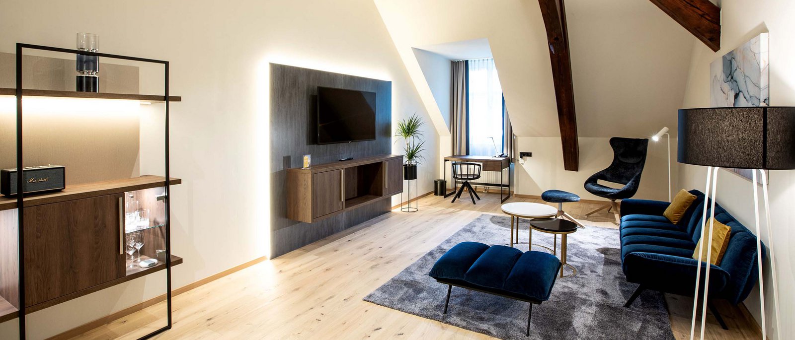 Executive Room Modernes Wohnzimmer mit blauem Sofa, Sesseln und Holzregal unter Dachschräge