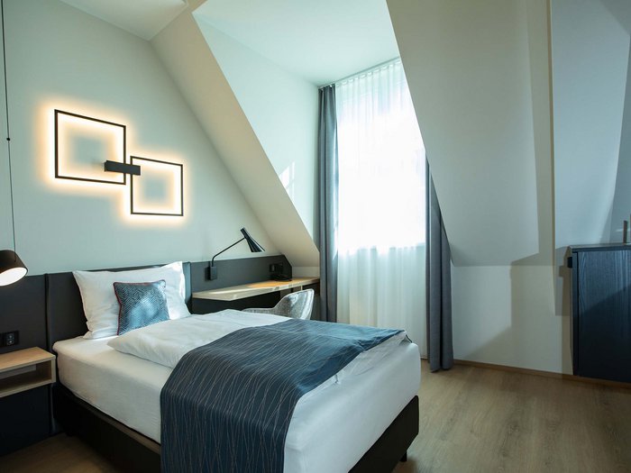 Hotel Böhlerstern in der Steiermark: unsere Zimmer Modernes Einzelzimmer mit Bett, Schreibtisch und dekorativer Wandbeleuchtung