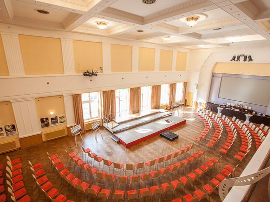 Seminarräume im Hotel Böhlerstern: der Theatersaal Leerer Konferenzsaal mit gebogenen Reihen roter Stühle und zentraler Bühne.