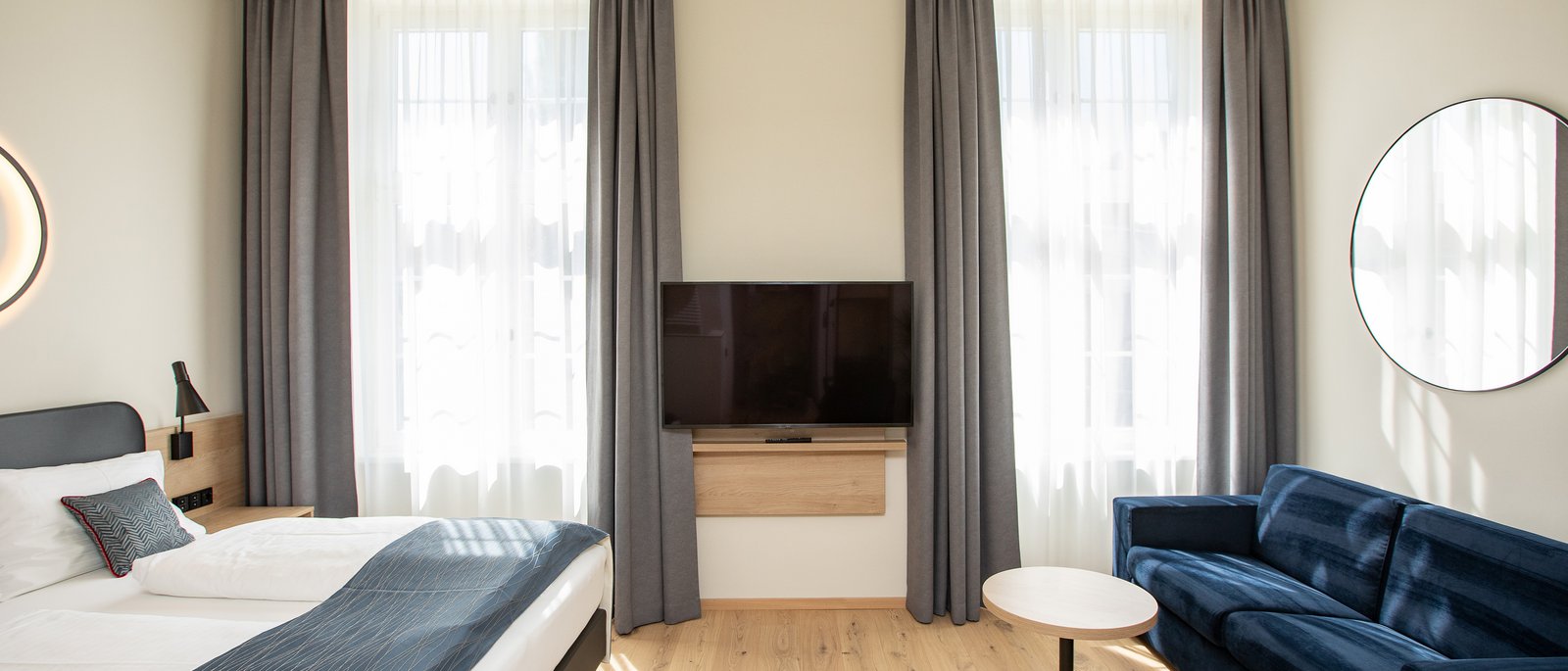 Deluxe double room Bright hotel room with double bed, blue sofa, and wall-mounted TV