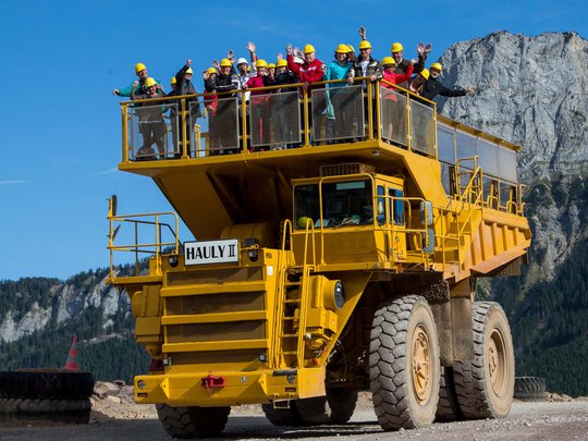 Our tips: the best trips in Styria Group of people wearing helmets standing on a large yellow dump truck with mountains behind