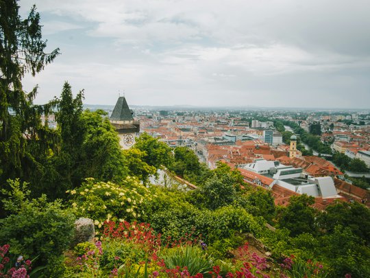 Our tips: the best trips in Styria View of Graz city with clock tower, red rooftops, and lush gardens in foreground