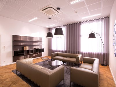 Executive Lounge Modernes Wohnzimmer mit beigen Sofas, runden Tischen und großen Fenstern mit Vorhängen
