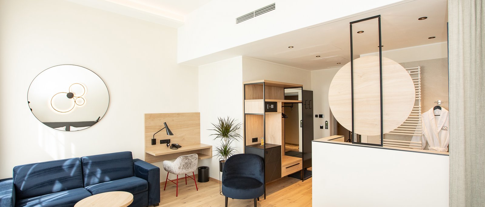 Deluxe double room Bright hotel room with blue sofa, desk, and open wardrobe