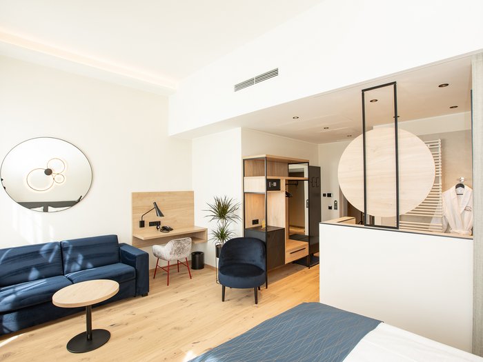 Hotel Böhlerstern in der Steiermark: unsere Zimmer Helles Hotelzimmer mit blauem Sofa, Schreibtisch und offenem Kleiderschrank