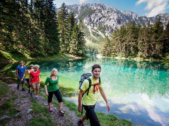 Our tips: the best trips in Styria Five hikers walking beside a clear mountain lake with tall pine trees in sunlight