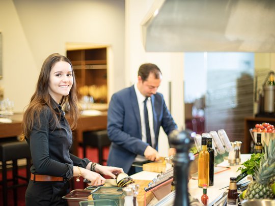 Seminar rooms at Hotel Böhlerstern: our Genusslabor® Young woman and man in suit chopping vegetables in modern kitchen.